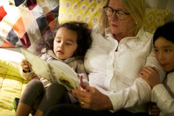 Abuela leyendo un libro a sus nietas mientras está acostado en la cama en casa